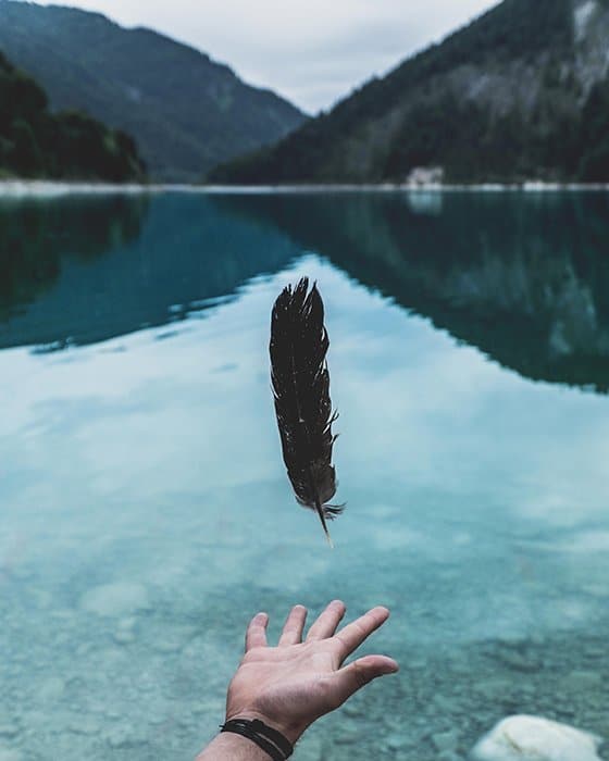 Una pluma levitando sobre una mano extendida con un hermoso paisaje de fondo: hermosos principios de fotografía