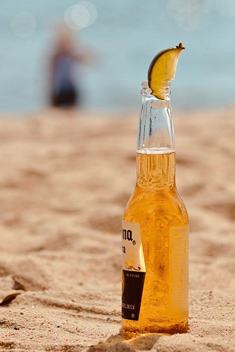 Una botella de cerveza corona con lima en una playa - cómo fotografiar cerveza
