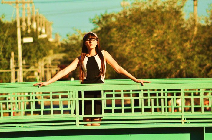 Un retrato de una modelo femenina posando en un puente verde con ángulos de cámara de tiro largo