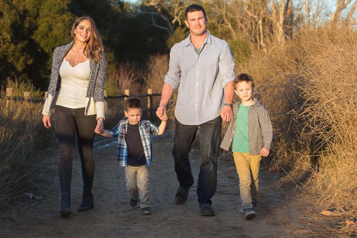 Un retrato de una familia de 4 sonriendo y tomados de la mano mientras camina en el campo