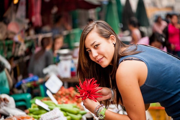 Una mujer morena con una camisa azul marino sin mangas sonriendo e inclinado sobre mercancías en un mercado fresco 