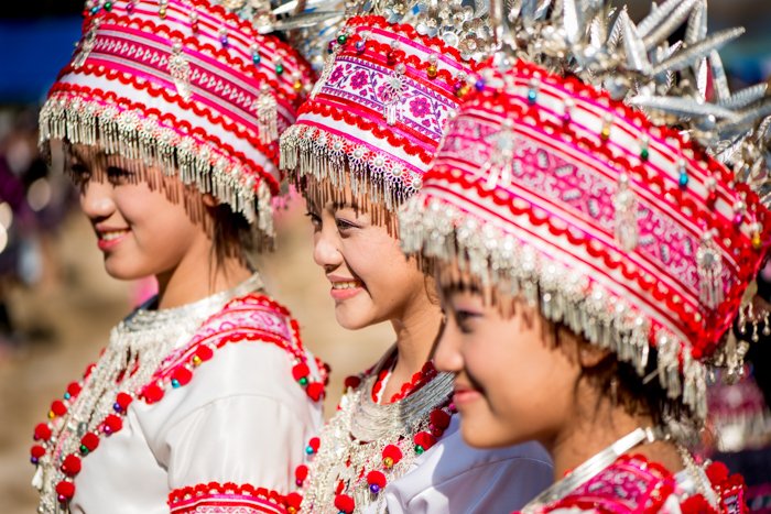 Tres niñas sonrientes vistiendo trajes y tocados tradicionales rojos y blancos