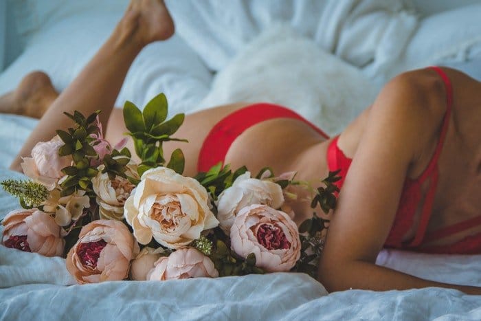 Un primer plano de una chica en lencería roja posando en una cama para una sesión de fotos de tocador nupcial