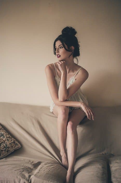 Una chica en lencería blanca posando en un sofá para una sesión de fotos de tocador nupcial