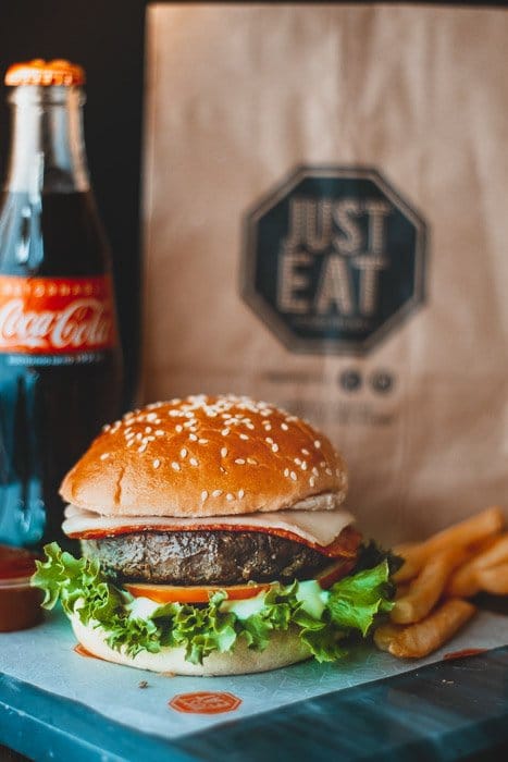 Una deliciosa hamburguesa junto a un refresco y una bolsa de papel para comida. 