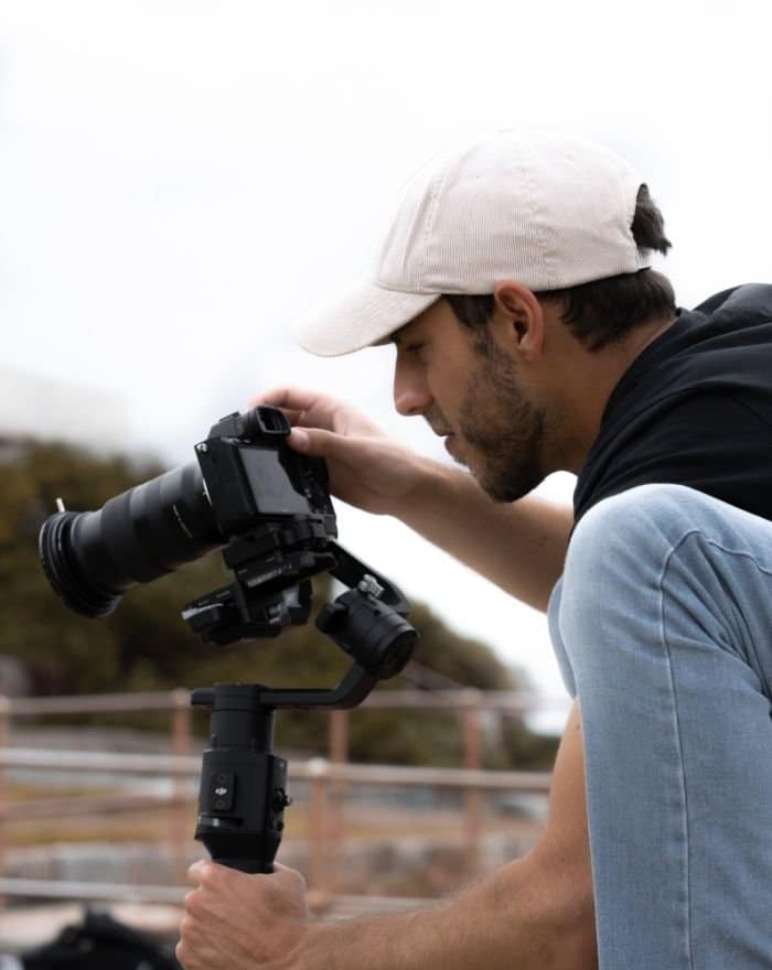 Hombre de camisa negra y jeans mirando a través de un visor de cámaras Dslr