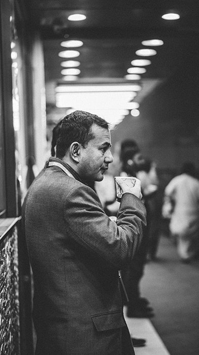 Una fotografía callejera franca en blanco y negro de un hombre tomando café en una estación de tren 