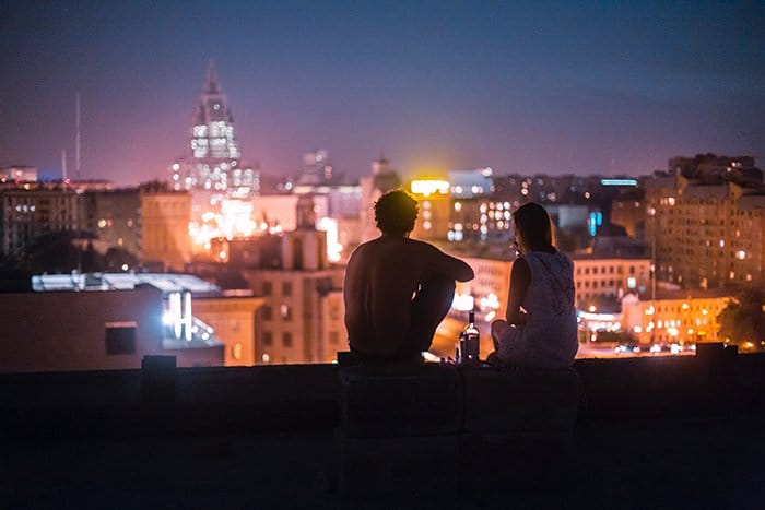 Un ejemplo de fotografía sincera de una pareja sentada en el techo de un edificio alto por la noche - 