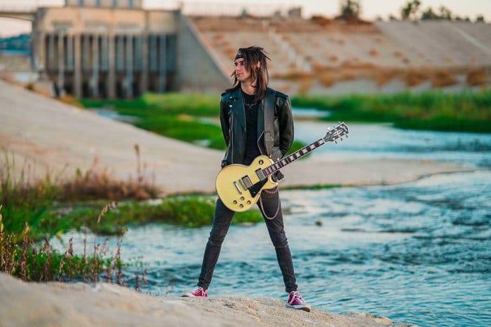 Un guitarrista de pie frente a un río. 