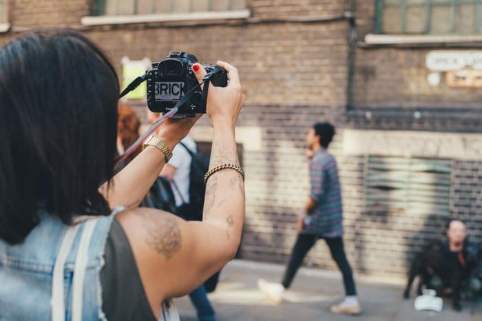 Una fotógrafa callejera sosteniendo una cámara réflex digital y tomando fotografías espontáneas de los transeúntes