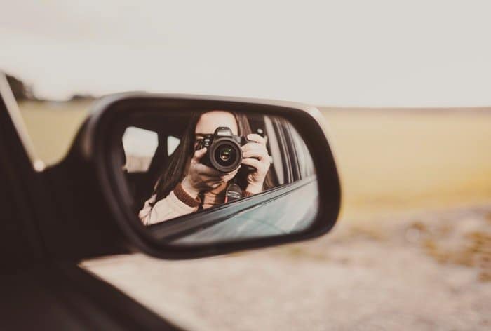 Una niña tomando un autorretrato en el espejo lateral de un coche