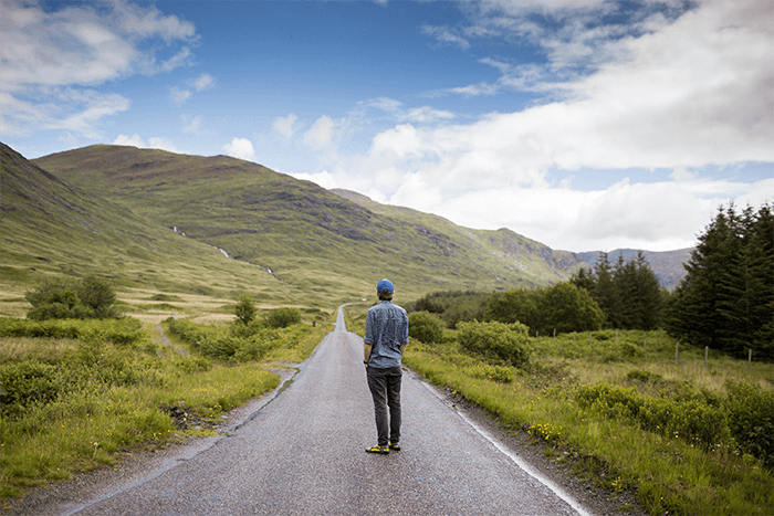 hombre parado en medio de una carretera entre un paisaje verde