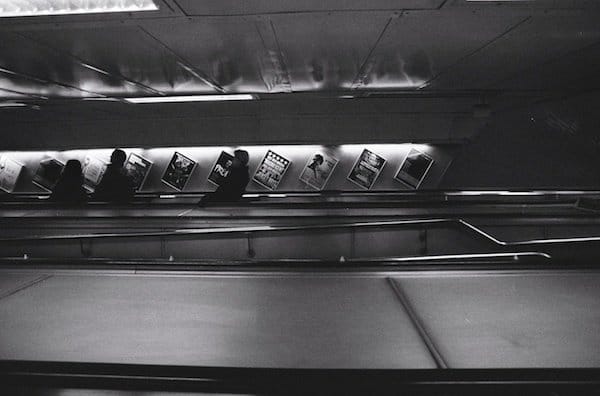 una imagen oscura de personas que viajan por las escaleras mecánicas subterráneas - fotografía callejera en blanco y negro