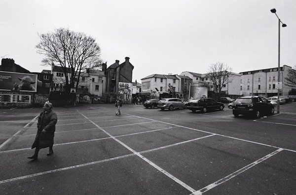 Una mujer camina delante de los coches en un aparcamiento - fotografía callejera en blanco y negro