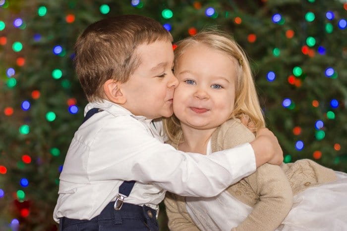 Dos niños pequeños abrazados con fondo borroso de luces de Navidad