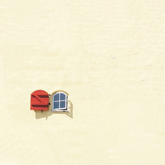 Fotografía de arquitectura minimalista: una imagen minimalista con una pequeña ventana con una contraventana roja abierta en una gran pared en blanco