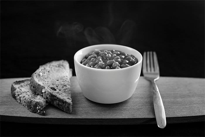 Una fotografía de alimentos en blanco y negro de frijoles horneados y pan en una bandeja de madera
