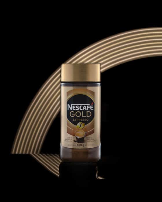 Fotografía de producto imagen de una botella de Nescafé tomada en un estudio con un arco iris dorado en el fondo