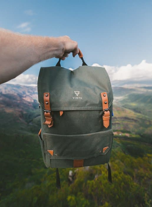 Imagen de fotografía de producto de una mochila sostenida contra un paisaje natural borroso de cielo, colinas y bosques