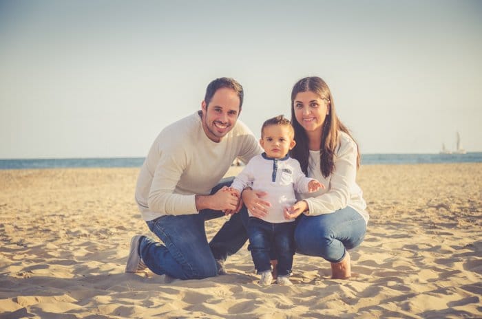 Una sesión de fotos familiar de una pareja y un bebé pequeño posando en la playa