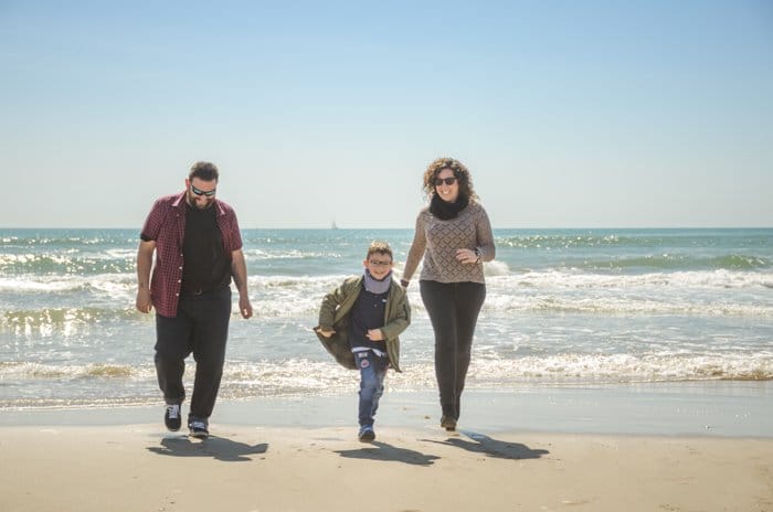 Foto de retrato de familia de una pareja y un hijo caminando en la playa 