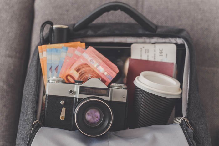 Mochila abierta con cosas necesarias para la fotografía de viajes como cámara, dinero, pasaporte y boletos