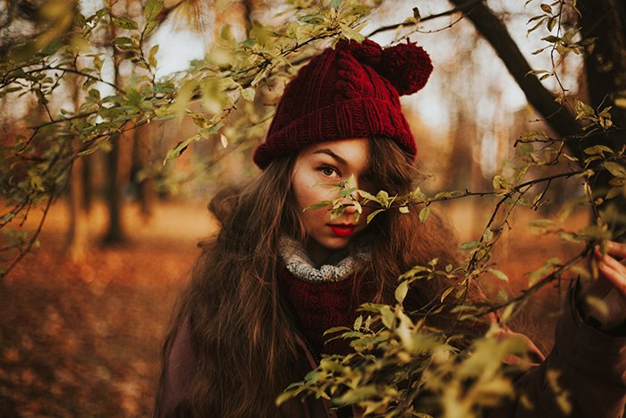 Retrato de una niña con sombrero rojo mirando a través de los árboles en un hermoso día de otoño - Retratos con luz natural
