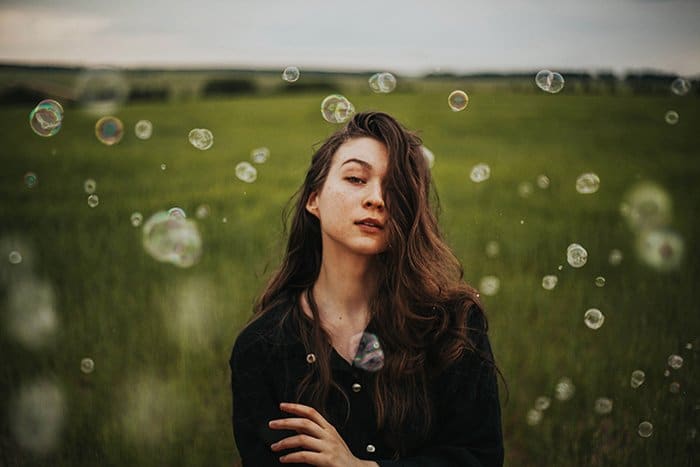 Retrato de luz natural de una niña de pie en campos verdes rodeados de burbujas