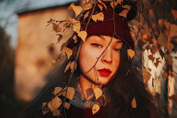 Luz natural retrato de niña con sombrero rojo mirando a través de los árboles en otoño