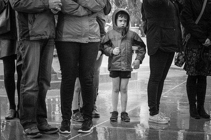 Fotografía callejera en blanco y negro de un niño en el centro de un grupo de adultos bajo la lluvia.  Consejos de fotografía callejera