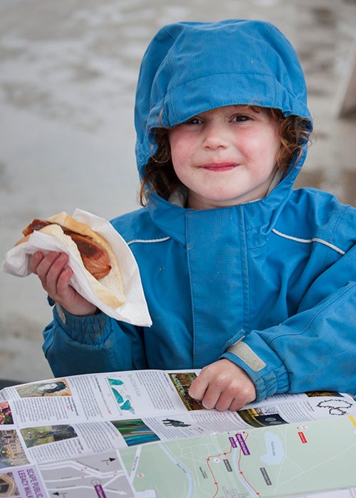 Fotografía de retrato de una niña en una chaqueta de lluvia azul sosteniendo un rollo de salchicha.  Consejos de fotografía callejera