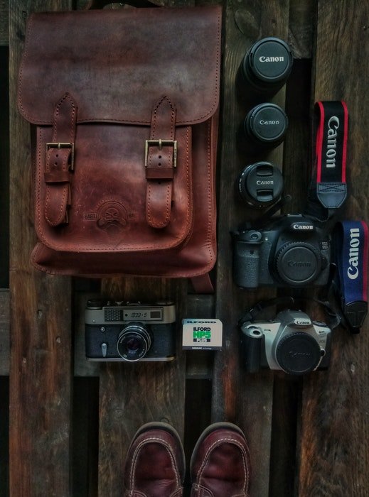 Una fotografía cenital de una bolsa de cuero para cámara y equipos esparcidos por una superficie de madera.