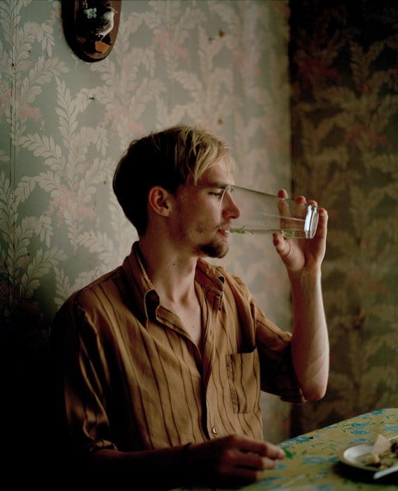 Sasha Arutyunova retrato de un hombre sentado en una mesa bebiendo de un vaso.  Fotógrafos de retratos famosos 