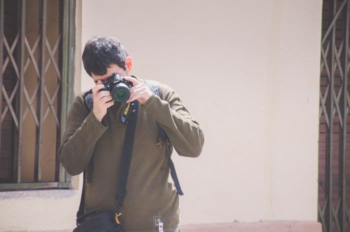 Foto de un hombre con un jersey verde oscuro que toma una foto con una cámara SLR Nikon durante una caminata fotográfica