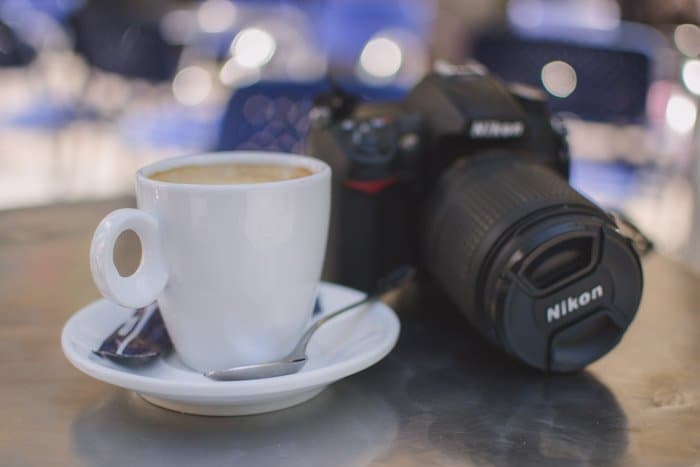Foto borrosa de una cámara Nikon y una taza de café con leche descansando sobre una mesa: ¡disfrute de su tiempo en su paseo fotográfico!