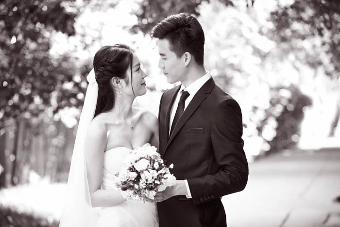 Retrato al aire libre de la novia y el novio asiáticos, felices y sonrientes, en blanco y negro.