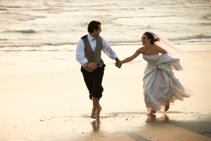 Una imagen del novio y la novia corriendo en la playa.