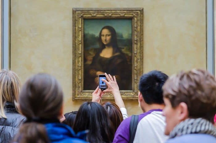 Multitudes frente a la pintura de Mona Lisa mientras un turista toma una foto con su teléfono inteligente