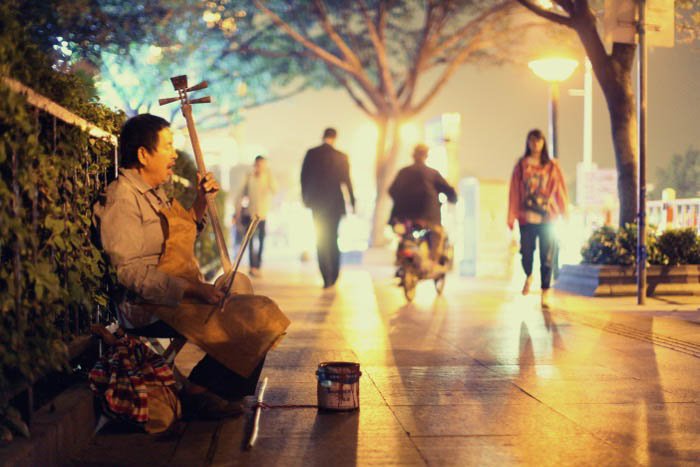 Un músico callejero tocando un instrumento de cuerda en la calle de la ciudad por la noche