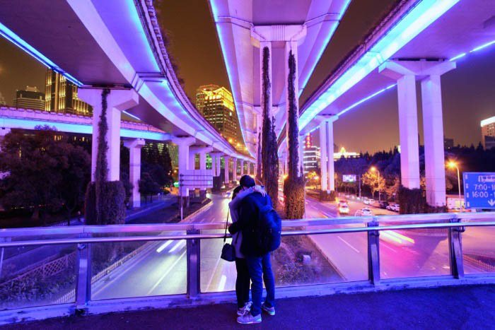 Fotografía nocturna de una pareja abrazándose bajo un puente moderno