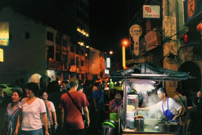 Una foto callejera nocturna de puestos de comida y transeúntes