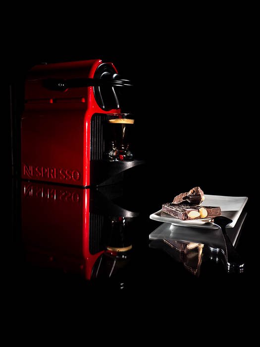 Una foto de estilo comercial de una máquina de café Nespresso junto a un plato pequeño de bombones