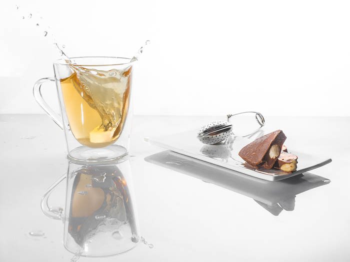 Una foto de comida minimalista de una taza de té salpicando junto a chocolates