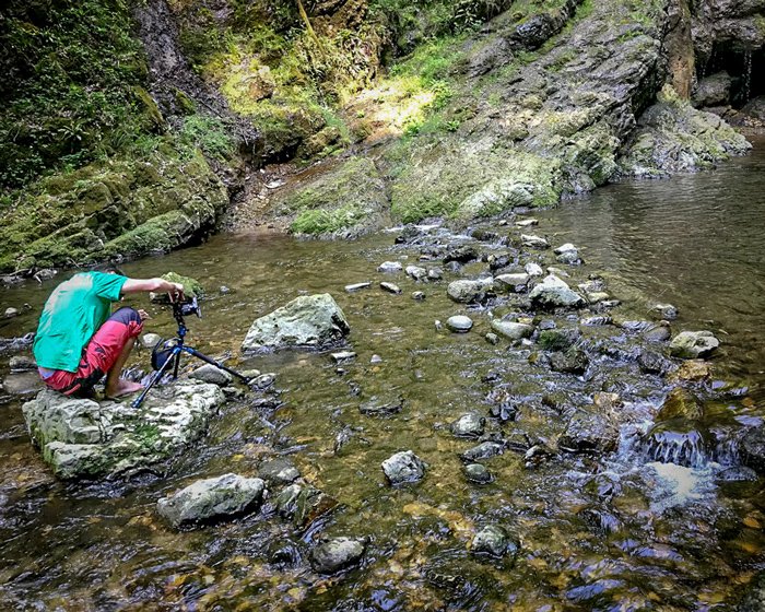 Un fotógrafo sentado sobre una roca con trípode y cámara para tomar imágenes en cascada
