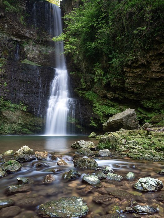 Una hermosa cascada que fluye rodeada de musgo verde y rocas.