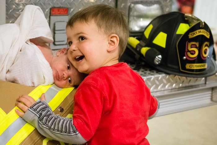 Un retrato de familia de un niño y un bebé recién nacido posados ​​con parafernalia de bombero 