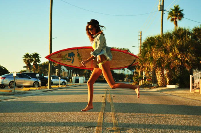 Una fotografía de moda de una modelo femenina caminando con una tabla de surf