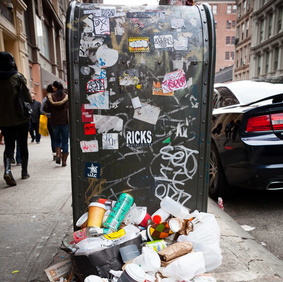 Fotografía callejera: buzón cubierto de graffiti y pegatinas con un montón de basura en primer plano
