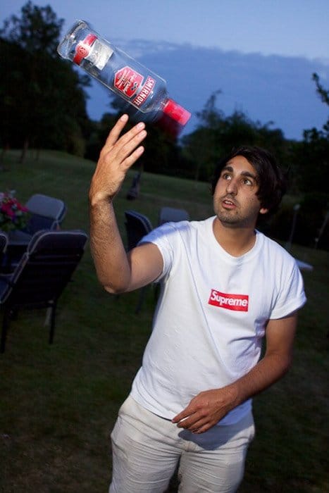 Un hombre haciendo malabares con una botella de vodka al aire libre con poca luz - Fotografía de fiesta