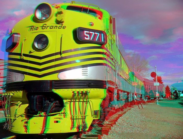 Fotografía anaglifo 3D de la parte delantera de un tren amarillo y sus vagones en las vías
